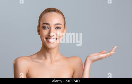 Femme souriante présentant le produit sur fond gris Banque D'Images