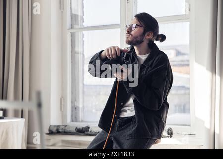 Portrait minimal de photographe masculin debout par la fenêtre et tenant l'appareil photo tout en donnant des instructions au modèle pendant le photoshoot, espace de copie Banque D'Images