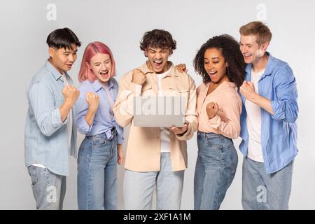 Groupe d'amis diversifié enthousiaste célébrant le succès sur ordinateur portable Banque D'Images