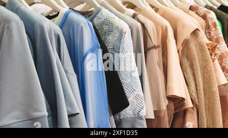 Une rangée de vêtements suspendus sur un rack, y compris une chemise bleue avec un motif de fleur blanche. Les vêtements sont soigneusement arrangés et semblent être à vendre Banque D'Images