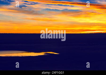 Beau coucher de soleil sur un champ avec un lac au premier plan. Le ciel est rempli de teintes orange et rose, créant une atmosphère sereine et paisible Banque D'Images