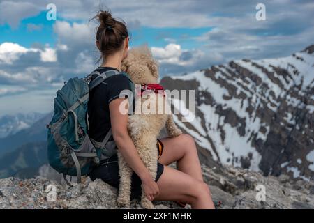 Une jeune femme est assise au sommet du pic Ha Ling, embrasse son chien et regarde le mont Lawrence Grassi. Banque D'Images