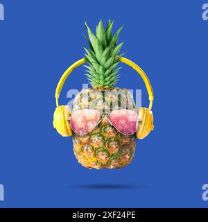 Ambiance estivale. Ananas avec lunettes de soleil et écouteurs sur fond bleu. Circulaire de fête ou autre article saisonnier Banque D'Images