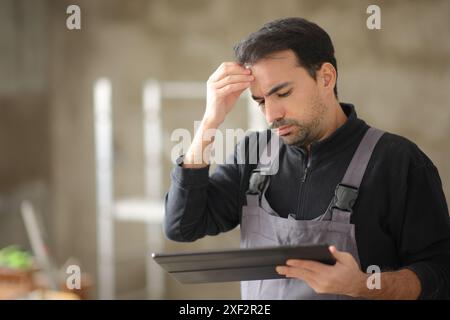 Travailleur de la construction inquiet vérifiant la tablette dans une maison Banque D'Images