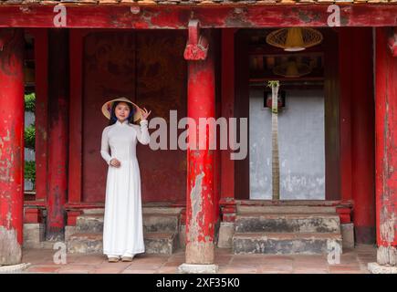 Jolie jeune femme vietnamienne portant une tunique traditionnelle Ao Dai et un chapeau conique au Temple de la littérature, Hanoi, Ha Noi, Nord Vietnam, Asie en juin Banque D'Images