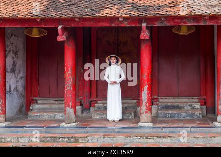 Jolie jeune femme vietnamienne portant une tunique traditionnelle Ao Dai et un chapeau conique au Temple de la littérature, Hanoi, Ha Noi, Nord Vietnam, Asie en juin Banque D'Images