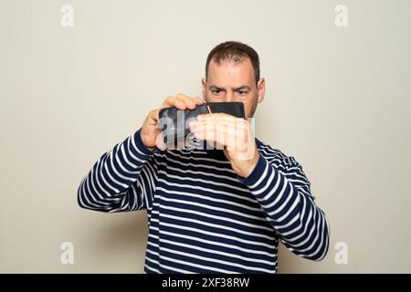 Triste homme espagnol montrant portefeuille vide à la caméra, pas d'argent, argent dépensé, fond de studio beige, espace de copie Banque D'Images