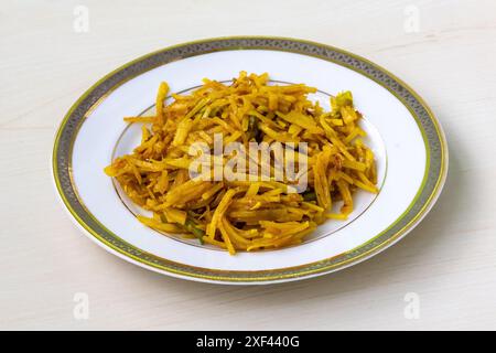 Délicieux aloo bhaji ou pommes de terre râpées frites dans une assiette blanche sur fond de bois. Authentique nourriture bengali qui est de fines tranches de pommes de terre frites Banque D'Images