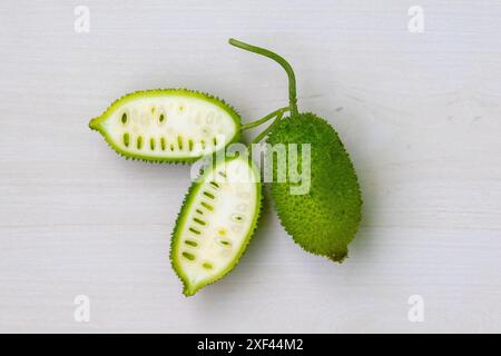 Légume vert de gourde épineuse tranchée et entière sur fond de bois blanc clair. Momordica dioica est également connu sous le nom de Kakrol, Kartoli, Kankoda, Kantola. Banque D'Images