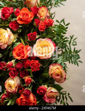 Partie d'un grand bouquet de roses rouges, oranges et jaunes avec des brins verts Banque D'Images