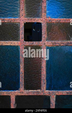 Vieille fenêtre encadrée en métal rouillé avec verre givré en bleu et marron Banque D'Images