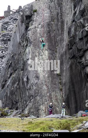 Grimpeur grimpant sur une paroi rocheuse de carrière d'ardoise à pic dans les carrières d'ardoise de Dinorwig près de Llanberis dans le nord du pays de Galles, pris en charge par deux compagnons ci-dessous Banque D'Images