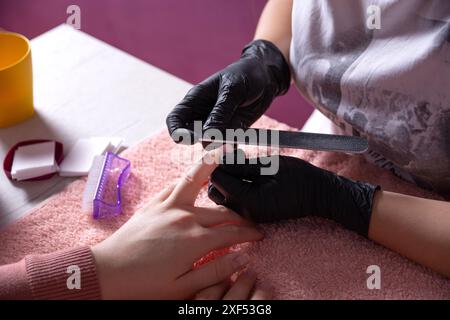 Gros plan d'une esthéticienne qui liait des clous pour sa cliente avec une lime à ongles dans son salon de beauté. Concept de manucure, de mode et de beauté Banque D'Images