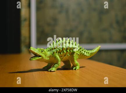 Une figurine d'un dinosaure vert avec des pointes se tient sur une table brune Banque D'Images