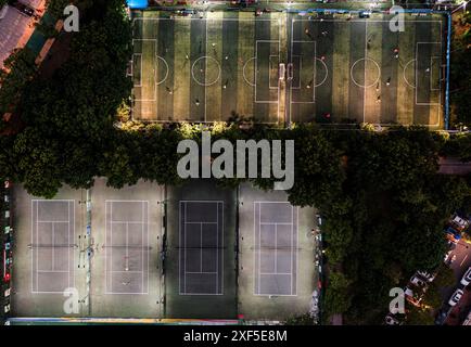 Une vue aérienne de terrains de football et de tennis illuminés entourés d'arbres la nuit dans la ville de Wuhan, en Chine Banque D'Images