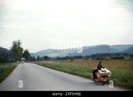 France. 1960 – Une jeune femme faisant une pause lors d’un voyage sur la route, s’assit sur un scooter Heinkel « Tourist » au bord de la route. Les bagages sont attachés à l'arrière du scooter. Banque D'Images