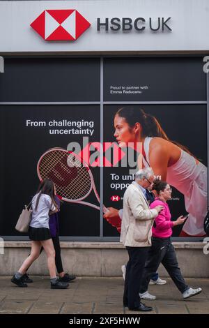 Wimbledon, Londres, Royaume-Uni 1er juillet 2024. Des piétons passent devant une succursale locale de la banque HSBC dans le centre-ville de Wimbledon avec une photo de la joueuse de tennis britannique Emma Raducanu en tant qu'ambassadrice de la marque mondiale. Credit : Amer Ghazzal/Alamy Live News Banque D'Images