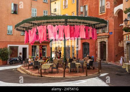 Café en plein air sur la place de la Poissonnerie avec des vêtements roses suspendus au-dessus, dans la vieille ville de Grasse sur la Côte d'Azur, Côte d'Azur, Provence, France Banque D'Images