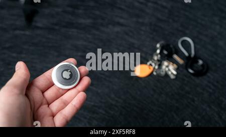 Jurmala, Lettonie - 25 06 2024 : la femme tient AirTag dans ses mains, et les clés de l'appartement sont floues en arrière-plan. Suivi de l'aide de l'étiquette aérienne Banque D'Images