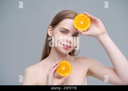 Une femme tient deux oranges dans ses mains et sourit. Concept de bonheur et de positivité, comme la femme pose avec le fruit dans un jeu et l Banque D'Images