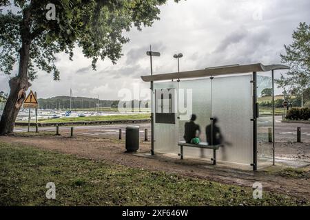 Abri de bus près du front de mer à vannes, Bretagne, France, avec deux personnes assises et des bateaux amarrés en arrière-plan. Banque D'Images