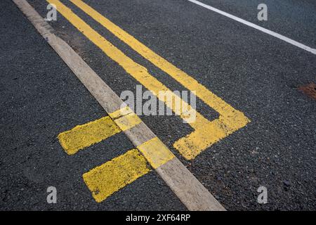 Vue rapprochée d'une double ligne jaune de restriction de stationnement peinte sur une route asphaltée avec bordure en béton. Banque D'Images