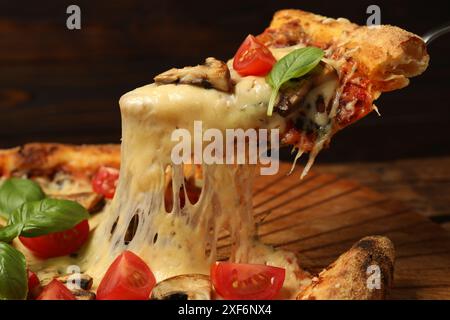 Prendre un morceau de pizza savoureuse avec du fromage fondu à la table en bois, gros plan Banque D'Images