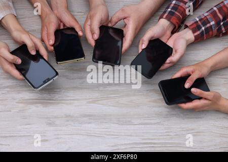 Personnes tenant des smartphones avec des écrans blancs à la table en bois, vue de dessus. Maquette pour le design Banque D'Images