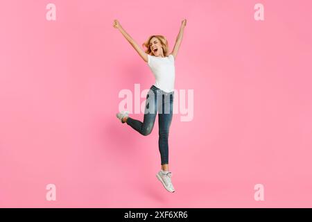 Heureuse jolie femme sautant dans l'air contre fond rose Banque D'Images