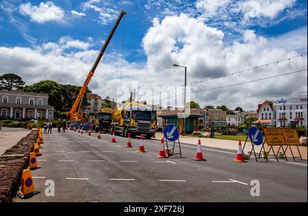 Travaux d'entretien sur rue urbaine avec grue et camion-citerne derrière des cônes de circulation sous ciel bleu et nuageux Banque D'Images