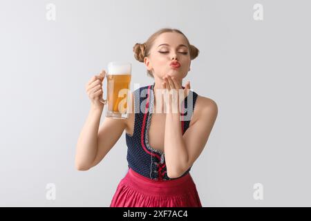 Magnifique serveuse d'octobre avec baiser soufflant de la bière sur fond clair Banque D'Images