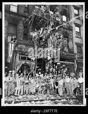 Des résidents exubérants de Little Italy à New York devant le 76 Mulberry St, saluent la nouvelle de l'acceptation japonaise des conditions de reddition alliées avec des drapeaux agités et une pluie de papier, New York, New York, 14 août 1945. Photo du New York World-Telegram et de la collection de photographies du journal Sun Banque D'Images