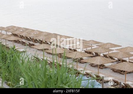 Plage vide avec parasols en paille et chaises longues en bois Banque D'Images