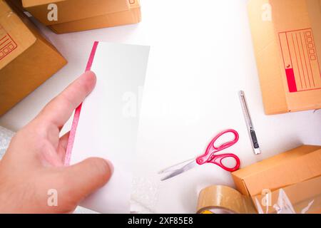 Facture blanche vierge dans une main avec des boîtes de marchandises pour l'emballage , concept de livraison de marchandises , vue de dessus Banque D'Images