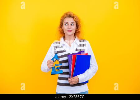 La recherche microscopique. Une femme professeur de biologie scolaire tient un microscope. Femme professeur de biologie. Retour à l'école. Professeur avec microscope sur jaune Banque D'Images