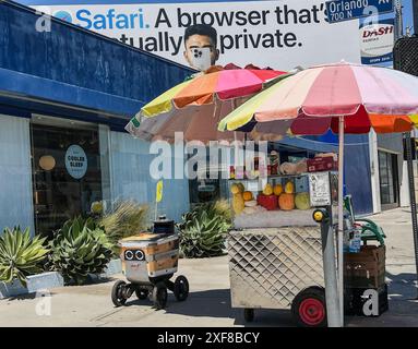 West Hollywood, Californie, États-Unis. 30 juin 2024. Oscar, un robot Axel 'Service Robotics' sans pilote, est vu conduire lui-même à travers West Hollywood le 30 juin 2024. Il s'est arrêté près d'un stand de fruits coloré, sous un panneau d'affichage qui montre un homme prenant une photo et un qui dit : 'Dashâ (Credit image : © Amy Katz/ZUMA Press Wire) USAGE ÉDITORIAL SEULEMENT! Non destiné à UN USAGE commercial ! Banque D'Images