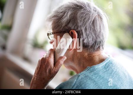 Norden, Allemagne. 30 juin 2024. Une dame de plus de 90 ans passe un appel téléphonique au 30.06.2024 à Norden (basse-Saxe). À maintes reprises, les personnes âgées sont victimes d'escroqueries téléphoniques. Une arnaque commune est le soi-disant appel de choc avec le truc de petit-enfant, dans lequel les fraudeurs téléphoniques trompent la personne âgée au téléphone en lui faisant croire qu'un petit-enfant ou un autre parent proche est en détresse. Crédit : Matthias Balk/dpa/Alamy Live News Banque D'Images