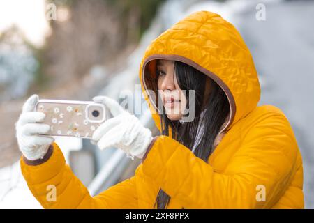 Une jeune femme prend une photo avec un téléphone portable dans un paysage enneigé Banque D'Images