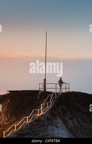 Lumière du soir au-dessus d'un personnage d'homme debout au sommet de Chapel Rock à la fin du brise-lames à Bude en Cornouailles au Royaume-Uni. Banque D'Images