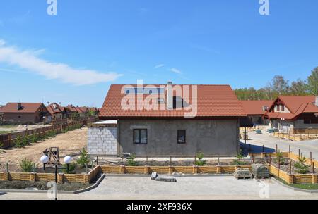 Gros plan sur le site de construction de maison avec clôture en briques, murs de plâtrage de maison, toit avec puits de lumière de grenier, chauffe-eau solaire de cheminée dans le chalet Banque D'Images