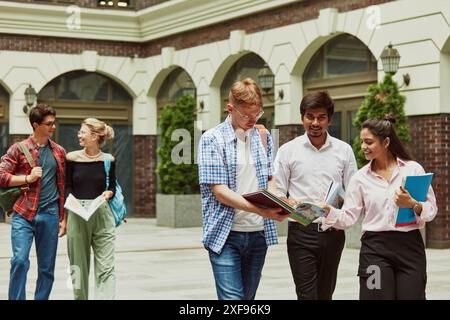 Étudiants de différentes nationalités, garçons et filles s'aidant mutuellement avec les devoirs à l'extérieur du campus. Discussion animée et assistance Banque D'Images