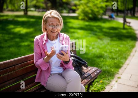 Portrait de femme mature dans le parc. Elle envoie des messages sur son smartphone. Banque D'Images