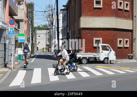 TOKYO, JAPON - 16 juin 2024 : une paire de personnes sur des vélos électriques de location Luup et un pilote sur un scooter électrique Luup sur une route dans la région de Meguro à Tokyo. Banque D'Images