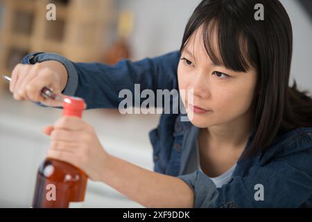 jeune femme essayant d'ouvrir une bouteille de vin Banque D'Images