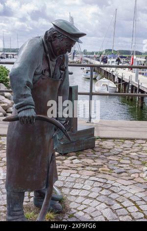 Statue en bronze d'un pêcheur au port, passerelle pavée et bateaux en arrière-plan, maasholm, allemagne Banque D'Images