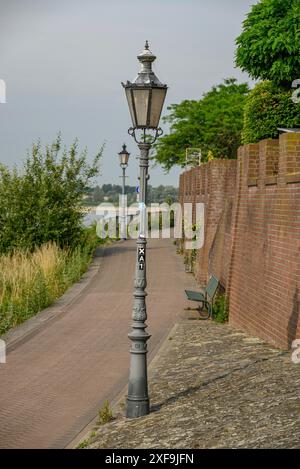 Un lampadaire se dresse le long d'un trottoir pavé à côté d'un mur de briques rouges avec des arbres et de l'herbe environnants, Rees. Allemagne Banque D'Images