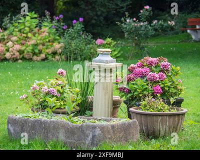 Scène de jardin fleuri avec divers pots de fleurs et une petite figure en pierre sur une pelouse verte, Spiekeroog, mer du Nord, Allemagne Banque D'Images