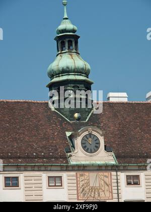 Vue détaillée d'une tour de l'horloge historique avec cadran solaire et flèche verte sur un toit, Vienne, Autriche Banque D'Images