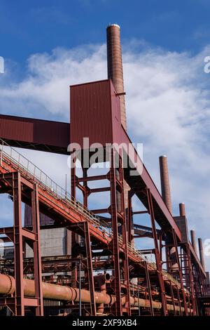 Usine industrielle avec plusieurs cheminées et construction en métal rouge devant un ciel bleu, essen. région de la ruhr, allemagne Banque D'Images