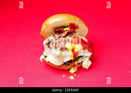 Hamburger au bœuf asturien. Burger brioche pain, oignon, fromage Becom, moutarde, ketchup, sur fond rouge. Espagne Banque D'Images